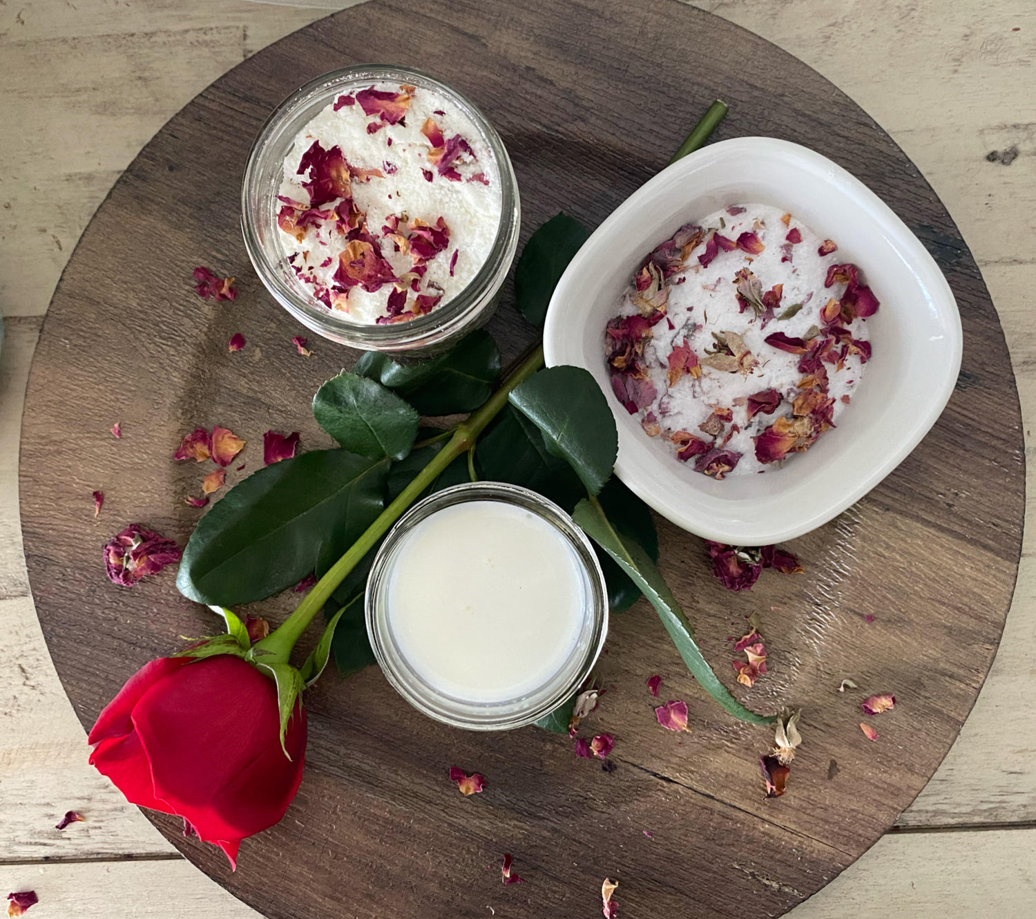 A new rose sits between elegant glass bowl containing rose & magnesium bath soaks and a cup of whole milk ready to enjoy a restorative warm bath.